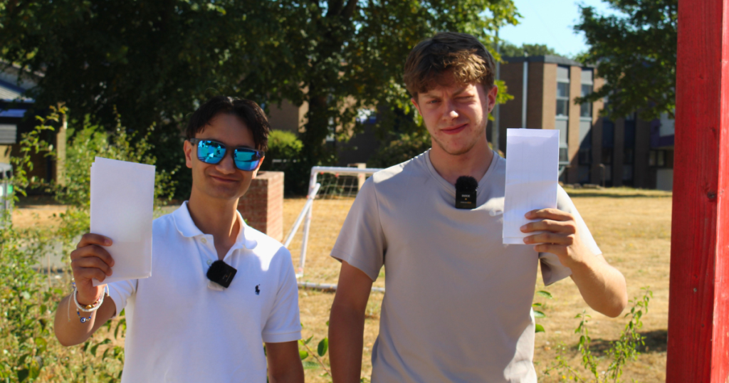 Two students holding up their grades. One is wearing sunglasses, they both have white tops on and brown hair.