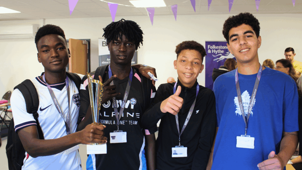 Four ESOL students smiling at the camera standing in a line. They all have dark hair.