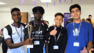 Four ESOL students smiling at the camera standing in a line. They all have dark hair.