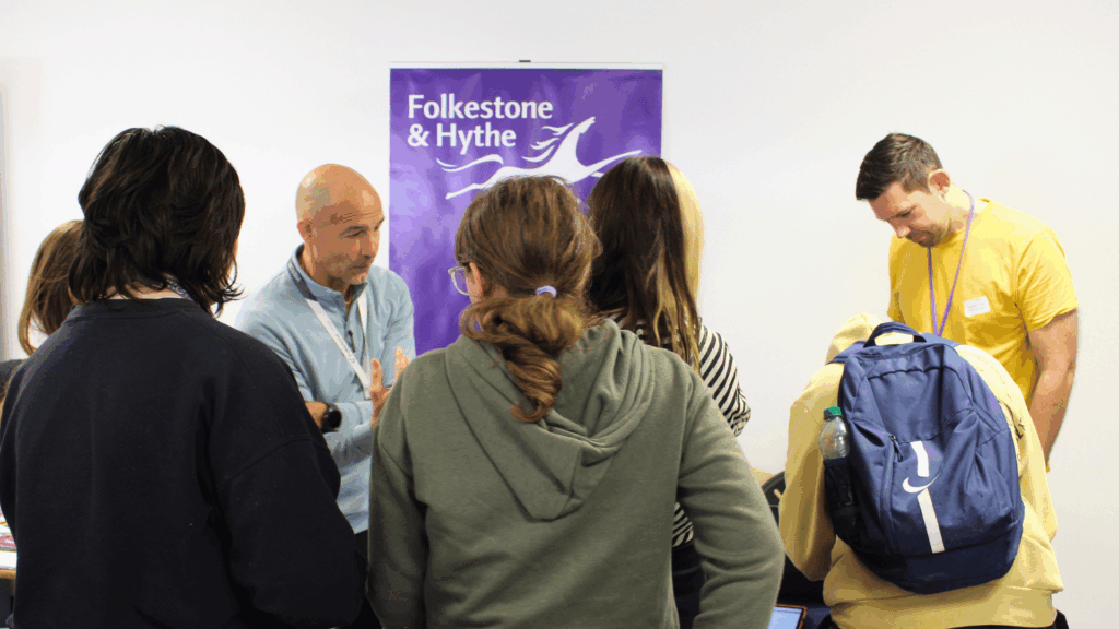 Students gathered around Folkestone and Hythe District Council's table talking to a man wearing a pale blue shirt.