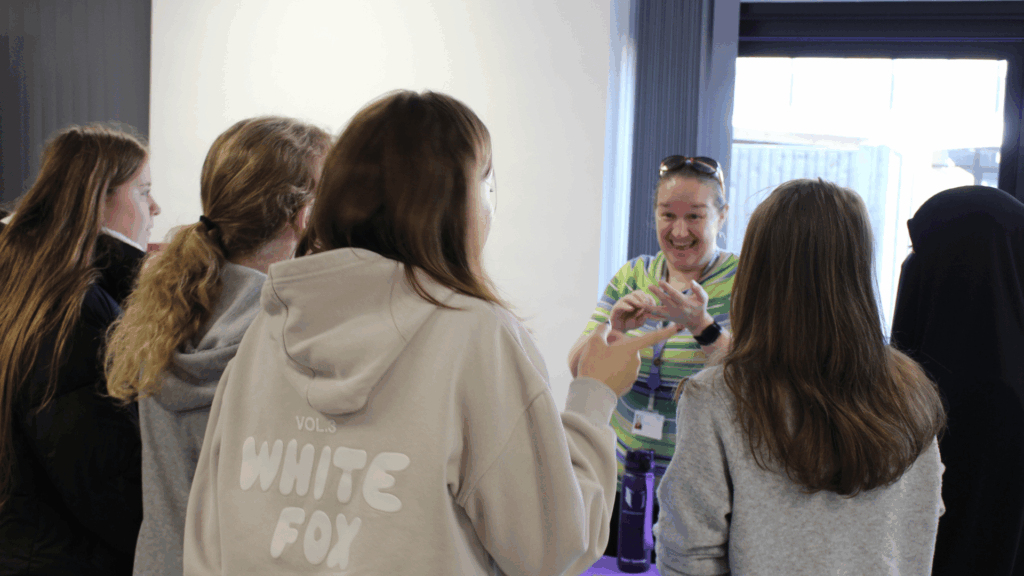 Students gathered around a college table talking to the Student Experience Officer, Debbie, who is smiling at them.