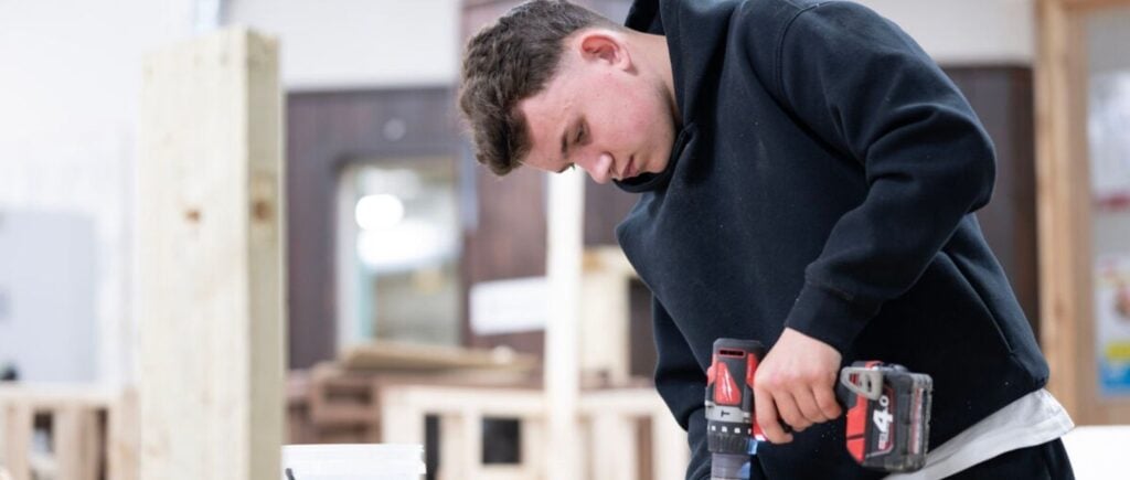 construction student using a power drill on a block of wood.