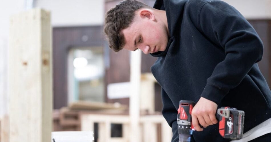 construction student using a power drill on a block of wood.