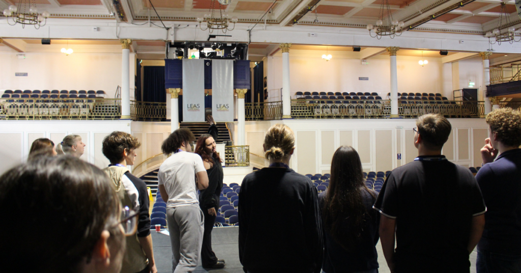 Students standing on the stage looking out into the grand hall area.